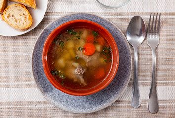 Appetizing light soup cooked in meat broth from potatoes, carrots, greenery with pork slices