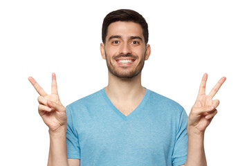 Fototapeta premium Young man standing in blue t-shirt, showing victory gesture with fingers of both hands