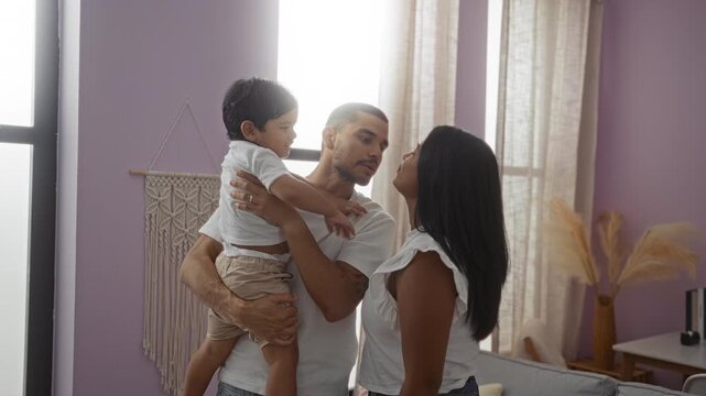 Family enjoying loving moment in modern living room with father holding young son as mother looks on smiling, showcasing love and togetherness indoors.