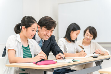 塾・学校の教室で先生に勉強を教わる小学生・中学生・高校生の子供（女の子）
