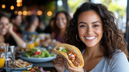 A woman with curly hair and a radiant smile is eating a taco surrounded by friends at a bustling restaurant, embodying joy and the pleasure of shared meals.