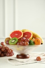 Glass vase with different fresh fruits and grapes on white table