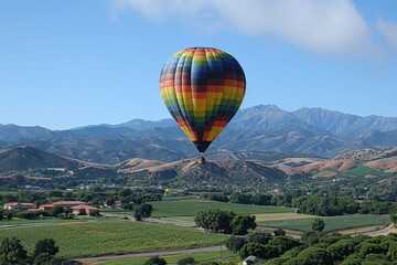 Obraz premium Colorful Hot Air Balloon Gliding Over Scenic Hills and Vineyards on a Clear Day