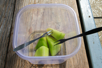 A close-up view of a small plastic container with pieces of green melon and two forks. A simple lunch of melon slices perfect for a picnic.