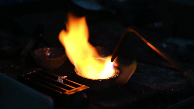 Close-up of skilled goldsmith heating and melting gold in crucible using torch, with bright flames