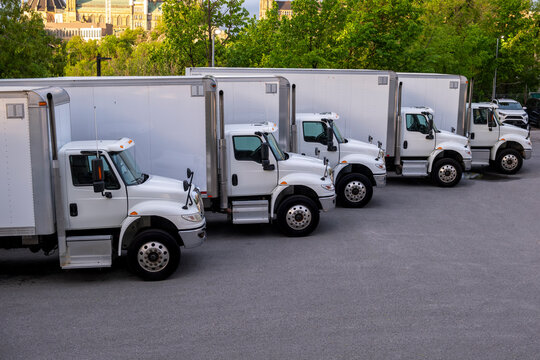 Multiple refrigerator cargo trucks in straight row at parking lot. Transportation, freight, supply chain, logistics, delivery, rising fuel prices concept.