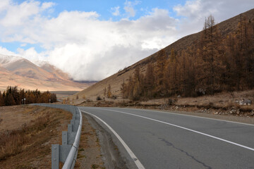 Left turn of the asphalt road with fences running along the hillside towards the beautiful mountain steppe on a sunny autumn day.