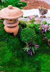 Minimal Japanese garden in home with small stone lantern and bamboo fountain and moss and flowers.
