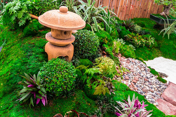 Minimal Japanese garden in home with small stone lantern and bamboo fountain and moss and flowers.
