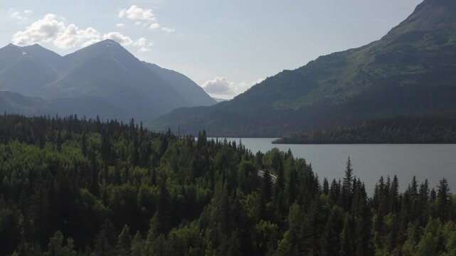 Aerial view of Upper Trail Lake with scenic mountain landscape and cars traveling on Seward Highway in the Kenai Peninsula of Alaska - 4K Drone