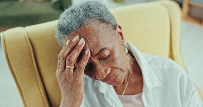 Stress, headache and sad senior black woman in a chair with memory or depression at nursing home. Anxiety, face and elderly African lady person in living room with dementia, Alzheimer or vertigo