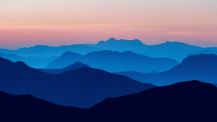 Illustrate a series of overlapping blue curves that form the silhouette of a distant mountain range at dusk.