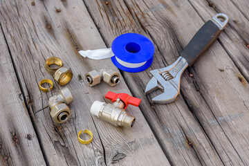 Different plumbing spare parts, sealing tape and adjustable wrench on a wooden background