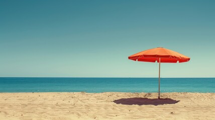 Red umbrella casting shade on sandy, quiet beach with blue ocean and sky