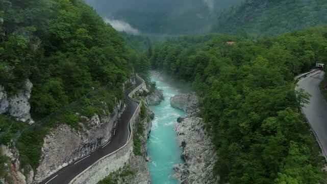 drone shot of the soca river in slovenia with blue water, a steet on the left site and trees around on a cloudy day