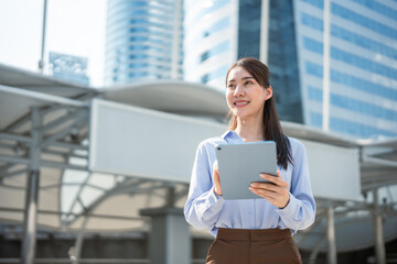 Fototapeta premium Asian young businesswoman using digital tablet while standing in the city. 