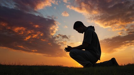 Fototapeta premium A silhouette of a young man on his knees in prayer, clasping his hands under a vibrant sunrise sky, symbolizing sacrifice and devotion.