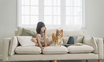Portrait of little asian girl stay home sit on the sofa  living room with lovely dog. Happy moment...