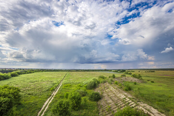 Lush green fields stretch endlessly beneath a vibrant sky, with clouds gathering, hinting at an...