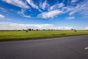 Golden hay bales dot the expansive landscape beneath a vibrant sky, as the sun casts a warm glow...