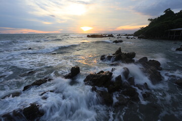 Long exposure of motion ocean wave crashing on the rocks in sunset background