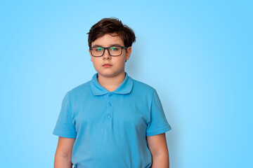 A calm dark-haired boy with glasses on a light blue background, looking into the camera