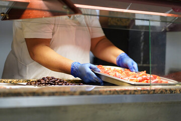 Female chef loads a table with food (tomatoes and olives) in metal plates for breakfast in a restaurant