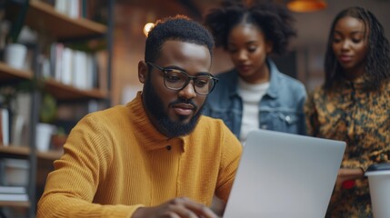 A man sits at a laptop, engaged with colleagues in an office environment