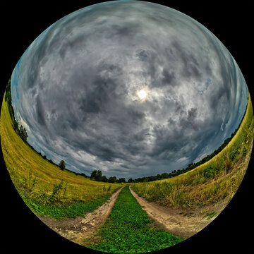 Wide angle panoramic view of a country road to a grassy meadow. Scenic landscape with dramatic sky on a cloudy summer day. Panorama shot through a circular fisheye lens in fulldome HDR photo format