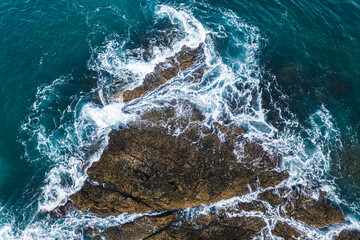 Aerial view of ocean waves crashing against rocks and creating a pattern of white foam, Close-up.