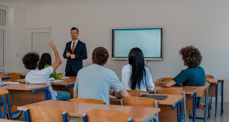 In the classroom group of college students listening to a university lecturer and engages in discussion and debate. Student raising a hand with a question for the teacher.