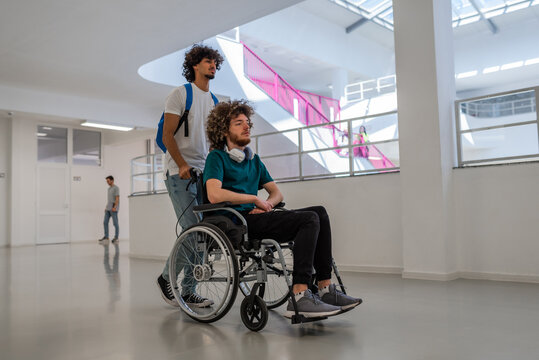 A group of happy diverse college students walking in the university hallway, a classmate pushing a friend in a wheelchair as they walk down the school corridor together. - Powered by Adobe