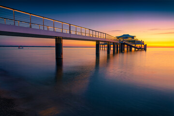 Fantastic morning seascape of Baltic sea. Dramatic summer sunrise on Wolkenlos Timmendorfer Strand  illuminated pier, Germany, Europe. Traveling concept background.