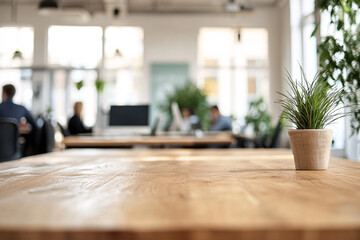 Empty Wooden Desk with Potted Plant in Bright Office with Blurred Professionals in Background