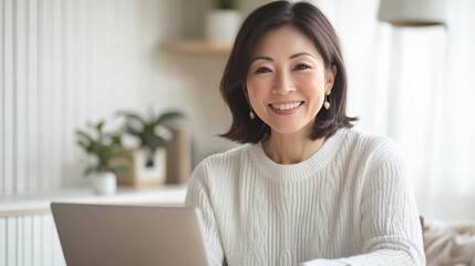 A young woman, smiling as she works on her laptop, is surrounded by a chic, minimalist home office interior in her beige shirt.
