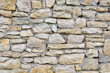 Background of a natural stone or sandstone masonry wall with cement in South France. Detailed stone texture image in beige, brown, grey and green	
