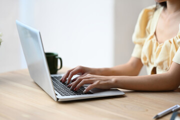 Fototapeta premium Close up image of unrecognizable young woman hands typing on laptop keyboard for searching information