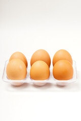 A row of light brown chicken eggs placed in a transparent holder, typically stored in the fridge. Photographed against a white background.