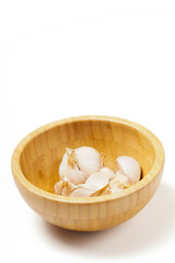 A wooden bowl filled with garlic (Allium sativum) ready to be used as a cooking ingredient. Photographed against a white background.
