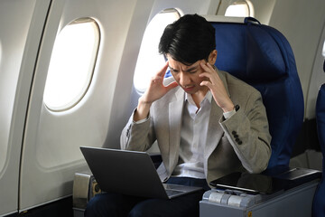 Young businessman having frustration or headache while working on his laptop in an airplane cabin