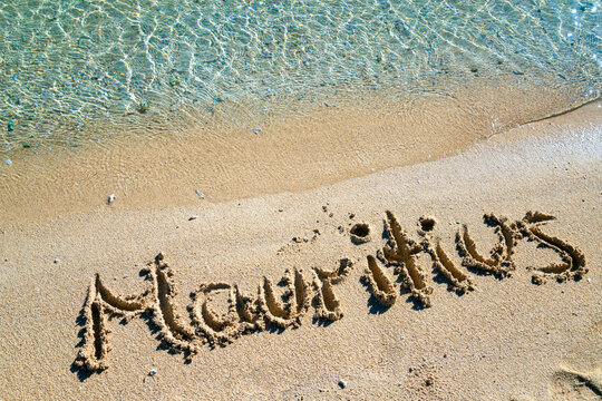 The word “Mauritius” written with a finger in the sand on the island's beach. Crystal-clear turquoise sea water, fine coral sand on the coast of the popular dream island in the Indian Ocean (Africa).