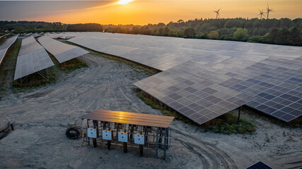 Industrial solar power station, currently under construction, showcasing solar modules and the array of white combiner boxes with power cables for connection to solar energy system grid.