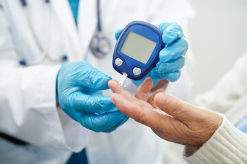 Asian doctor using digital glucose meter for check sample blood sugar level to treatment diabetes.