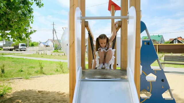 Adorable little girls plays on the playground. A children slides down a slide. Happy childhood concept