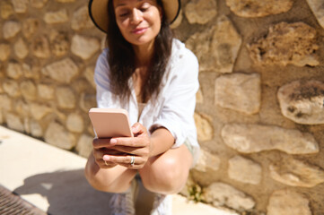 Young woman using smartphone outdoors by stone wall on a sunny day