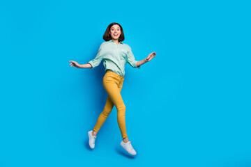 Full length photo of elegant graceful lovely cute woman dressed teal shirt yellow trousers jumping isolated on blue color background