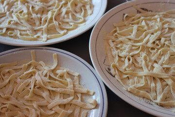 Homemade italian traditional Tagliatelle pasta on  plates with flour.. Raw itialian pasta also called fettuccine, tagliatelle or pappardelle