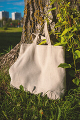 White canvas tote bag mockup template with long handles among the green plant leaves outdoor