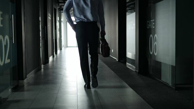 Silhouette of a businessman walking alone down a dark office hallway.