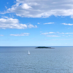 Fototapeta premium Yacht sailing along the island in the Baltic Sea with a blue sky and clouds near Vattuniemi, Helsinki, Uusimaa, Finland, August 2020